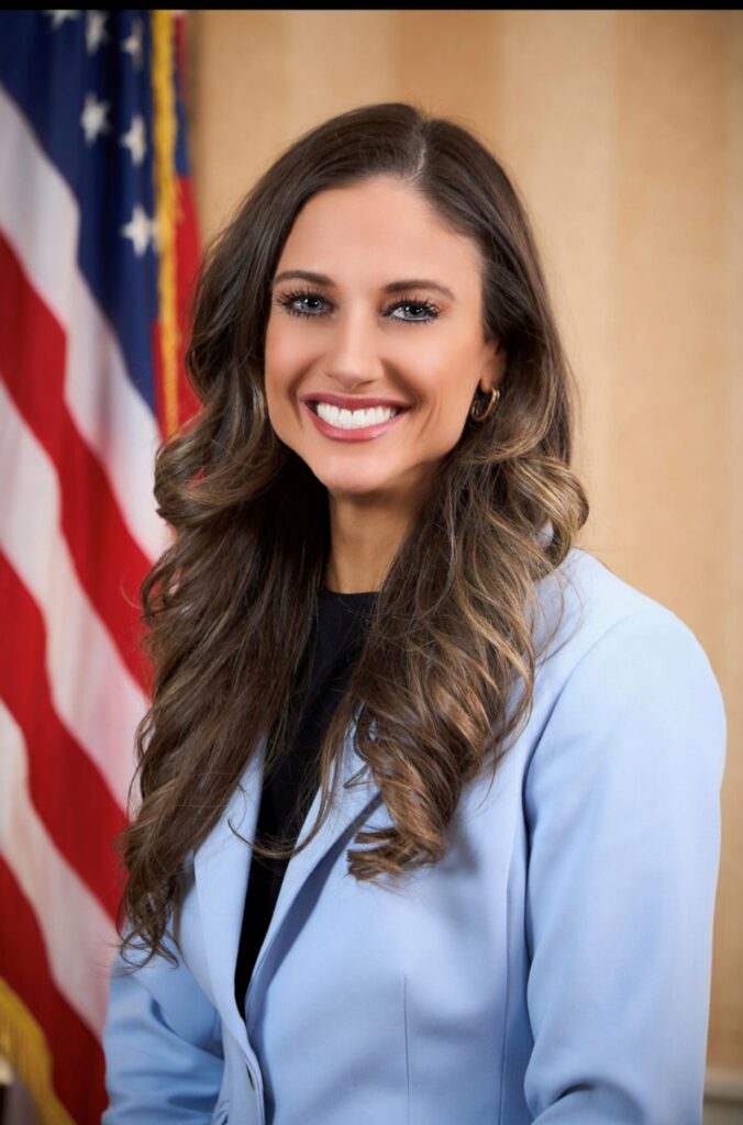 Chelsey in blue inside smiling next to american flag